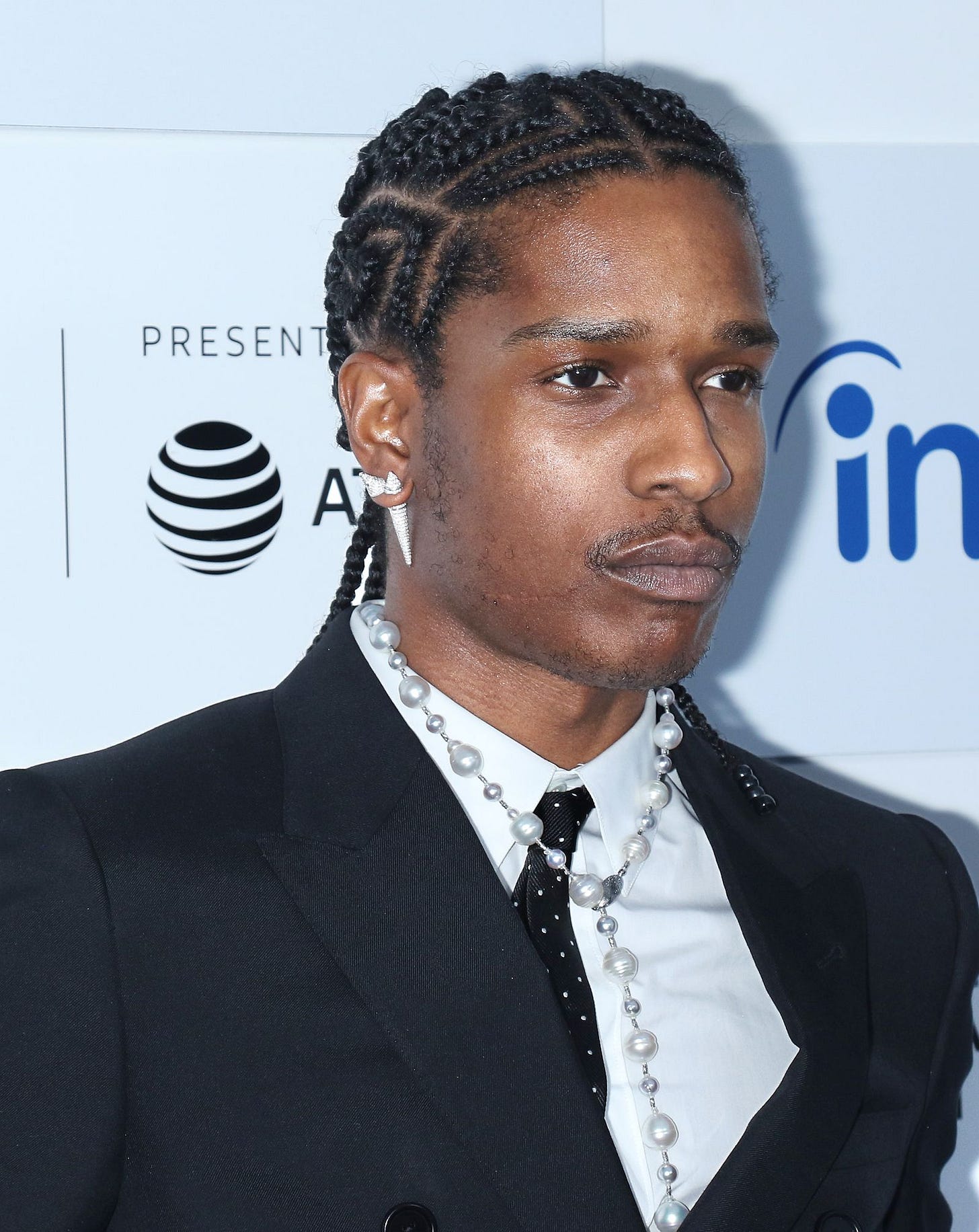 man with zigzagging braids and thin moustache wearing a pearl necklace diamond spike earrings and a suit man with zigzagging braids and thin moustache wearing a pearl necklace diamond spike earrings and a suit