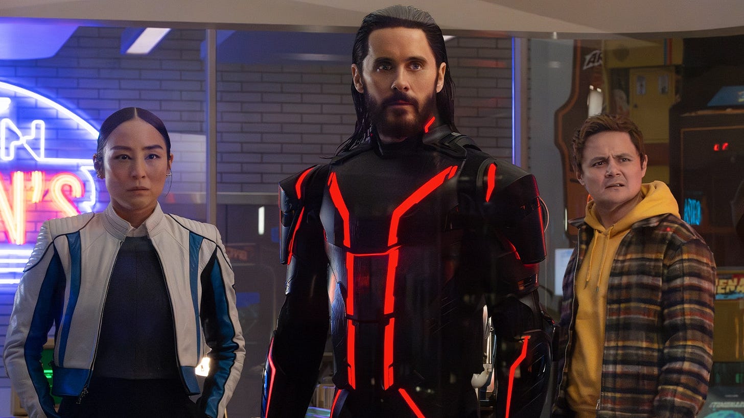 From left to right: Eve (Greta Lee), Ares (Jared Leto), and Seth (Arturo Castro) looking concerned off-screen in Flynn's office. From left to right: Eve (Greta Lee), Ares (Jared Leto), and Seth (Arturo Castro) looking concerned off-screen in Flynn's office.