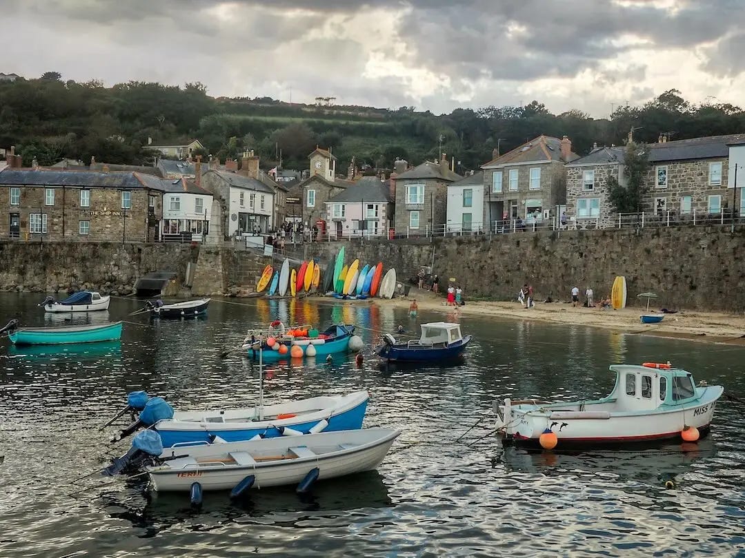 Small fishing boats in a harbour with a wall and cottages behind