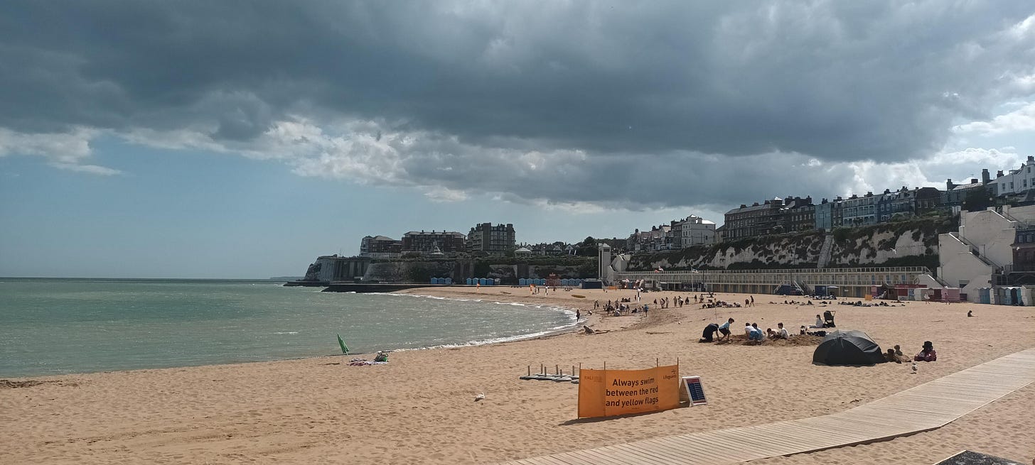 View of Broadstairs, sandy beach in the foreground and the seafront behind with heavy grey skies overhead