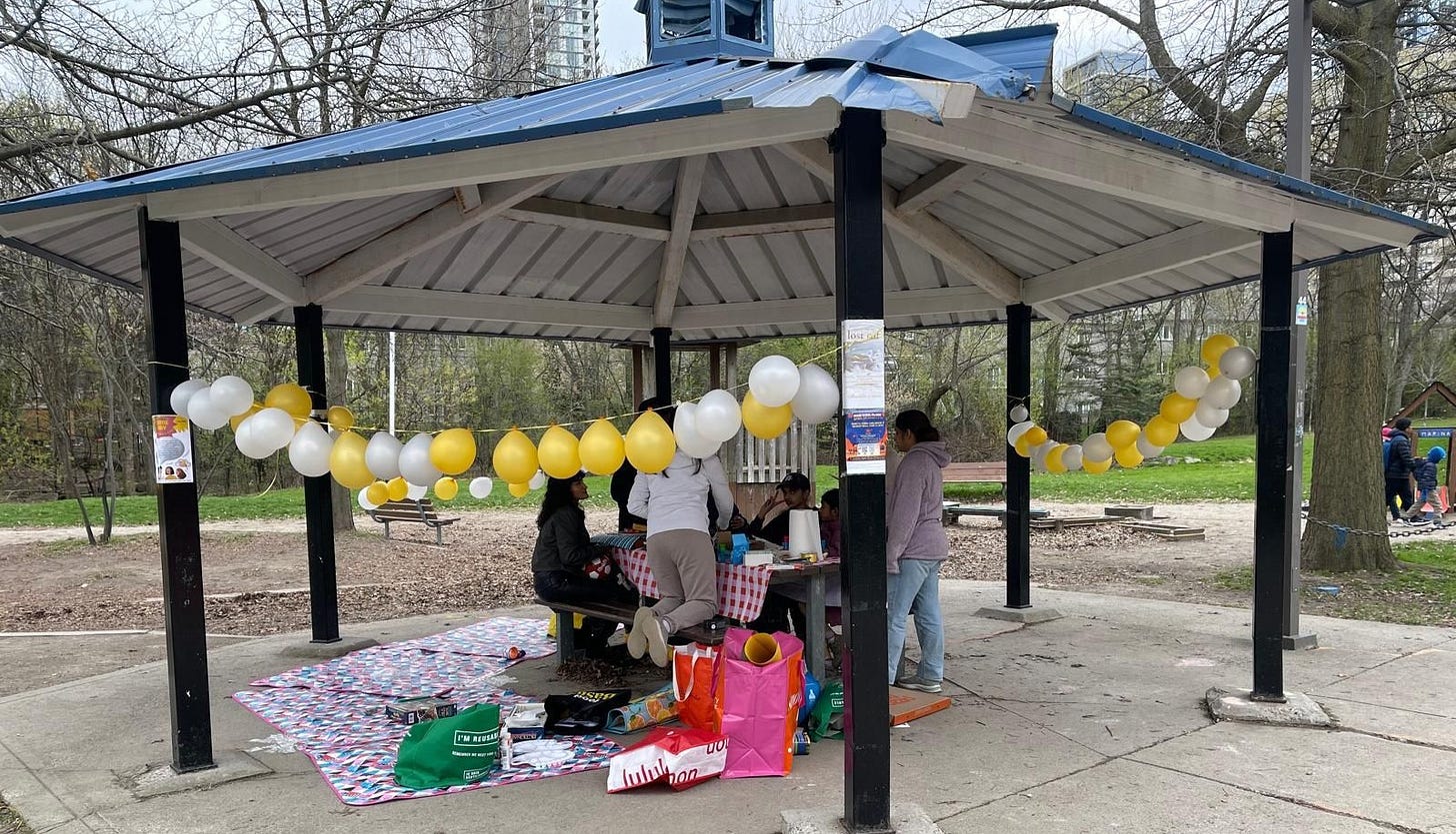 Group sat around a table, under a bandstand, with balloons and food, talking