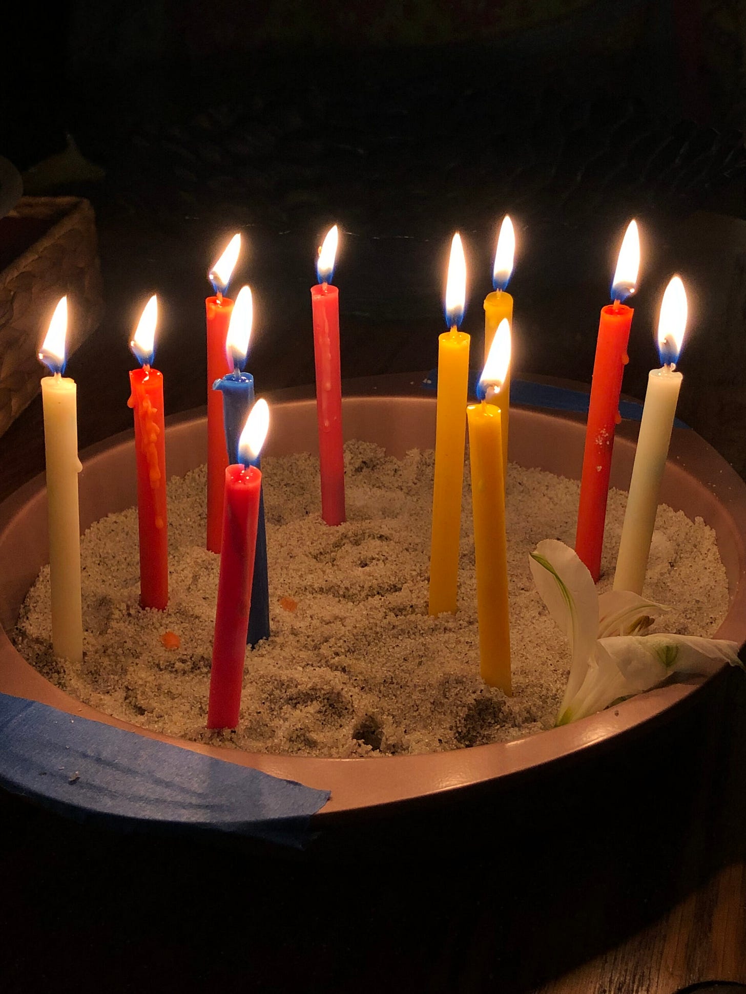 Many colored candles burn in the darkness while set in a bowl of sand. Many colored candles burn in the darkness while set in a bowl of sand.