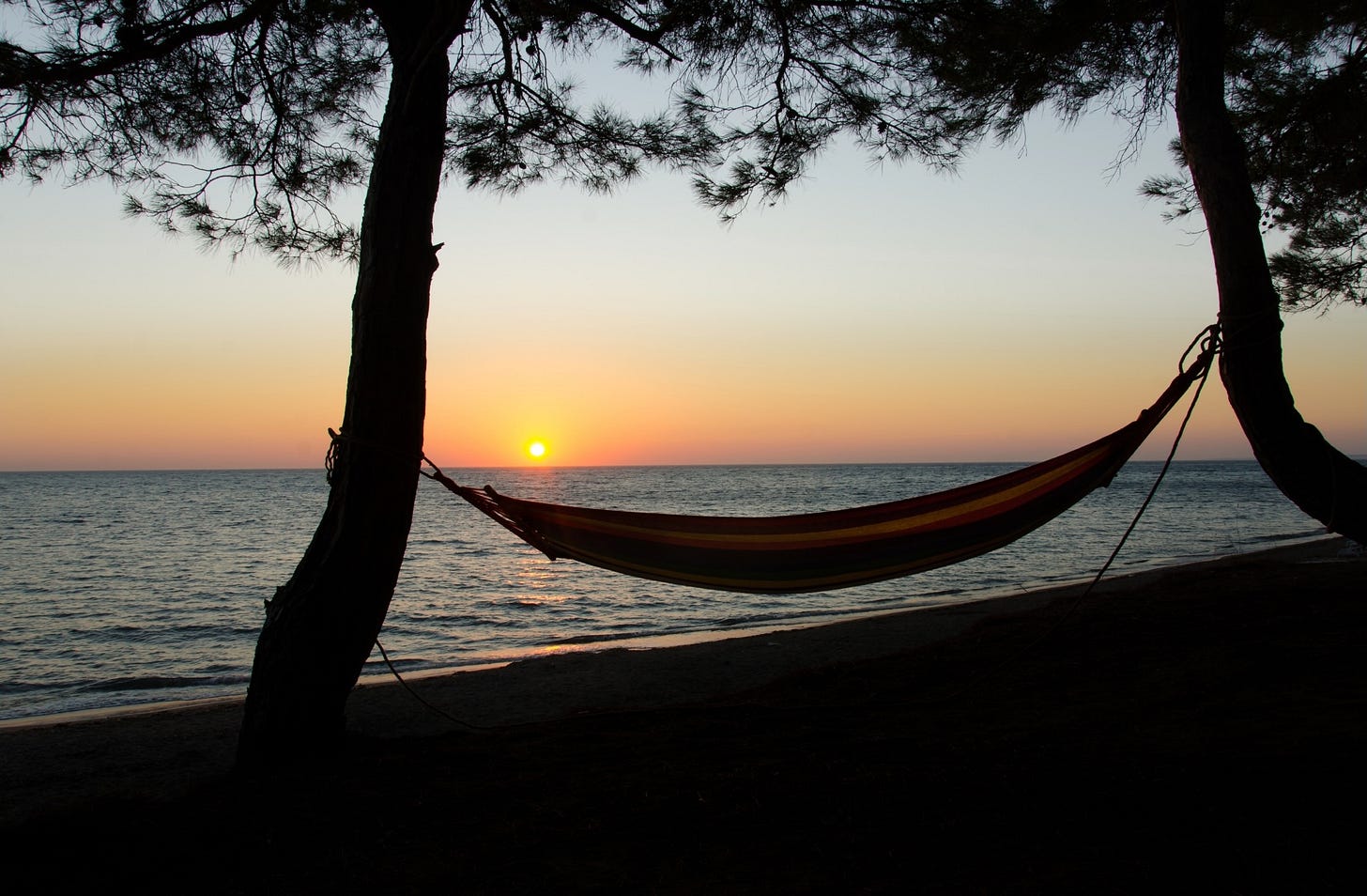 A hammock overlooks the sun setting on the ocean.