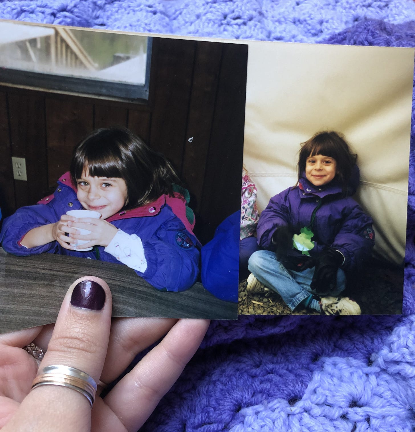 an image of a left-handed white person thumb with a silver ring and a dark purple painted nail, holding two photographs of Lena as a child on a camping trip. they are about eight years old, have a brown bowl cut with bangs, and are wearing a purple puffy jacket. an image of a left-handed white person thumb with a silver ring and a dark purple painted nail, holding two photographs of Lena as a child on a camping trip. they are about eight years old, have a brown bowl cut with bangs, and are wearing a purple puffy jacket.