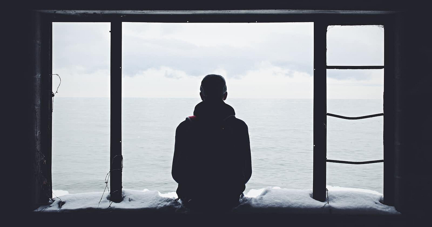 Solitary figure sitting on a snow-covered ledge, overlooking water and sky through a large window, symbolizing the loneliness and heartache of unrequited love.