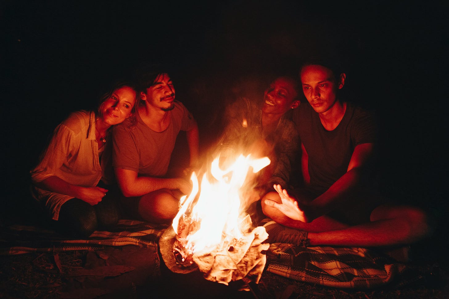 Four people sitting around a campfire at night. 