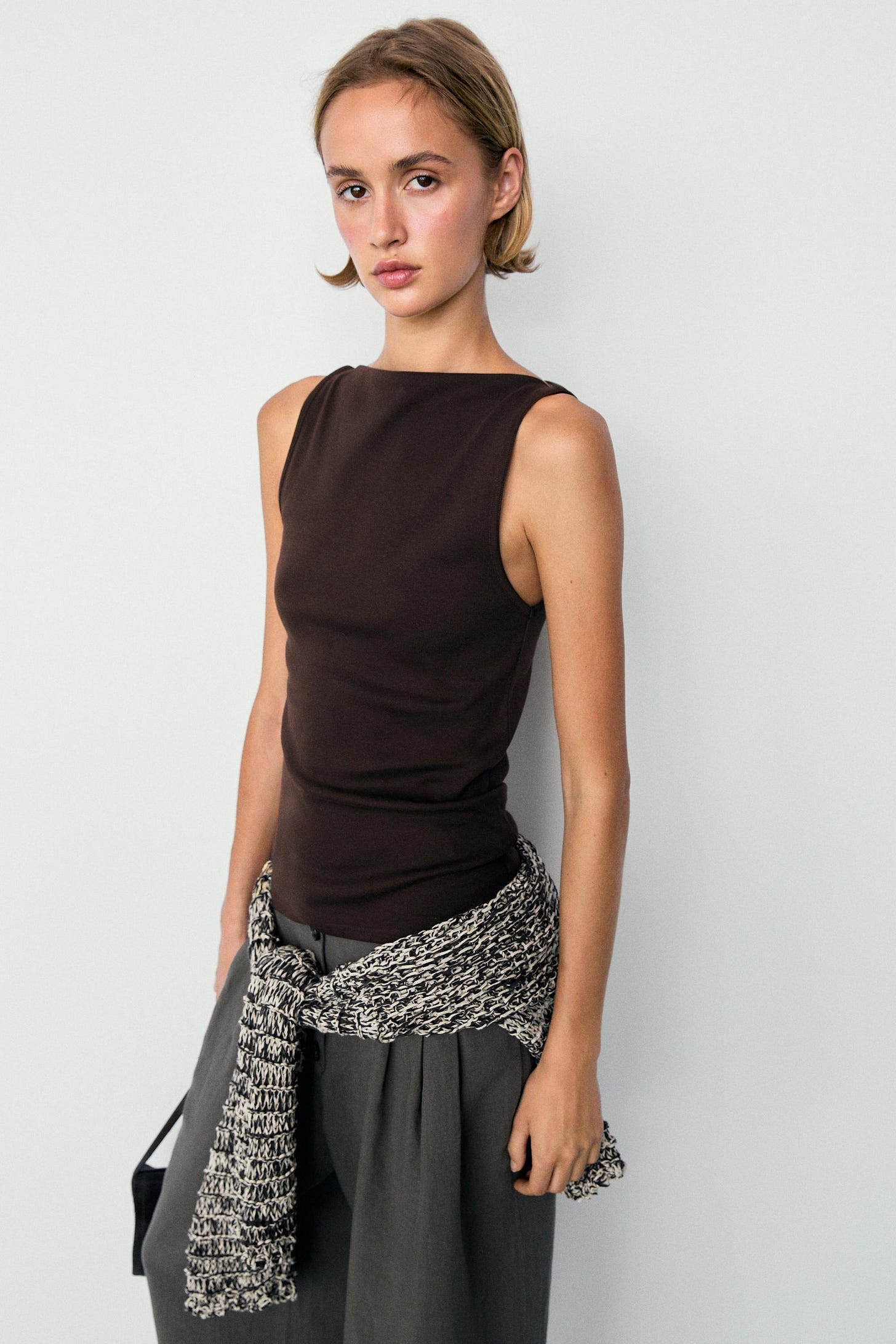 Ensemble composé d'un débardeur marron à encolure droite, d'un pantalon gris et d'un pull noué à la taille.