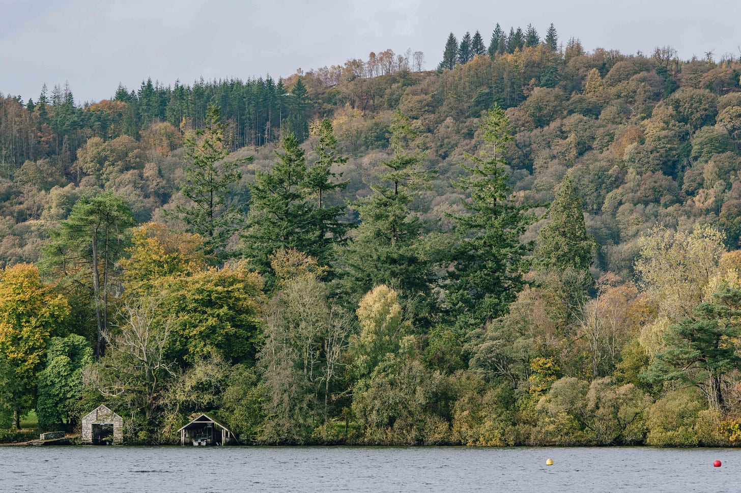 Tree-lined lake shore with stone boathouse and autumn foliage in the Lake District, Cumbria, England, nature and landscape photography. Tree-lined lake shore with stone boathouse and autumn foliage in the Lake District, Cumbria, England, nature and landscape photography.