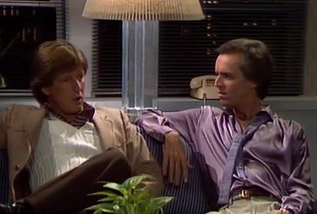 WKRP's Andy Travis sits casually dressed on a sofa next to radio consultant Norris breeze, who is wearing a shiny violet dress shirt. WKRP's Andy Travis sits casually dressed on a sofa next to radio consultant Norris breeze, who is wearing a shiny violet dress shirt.