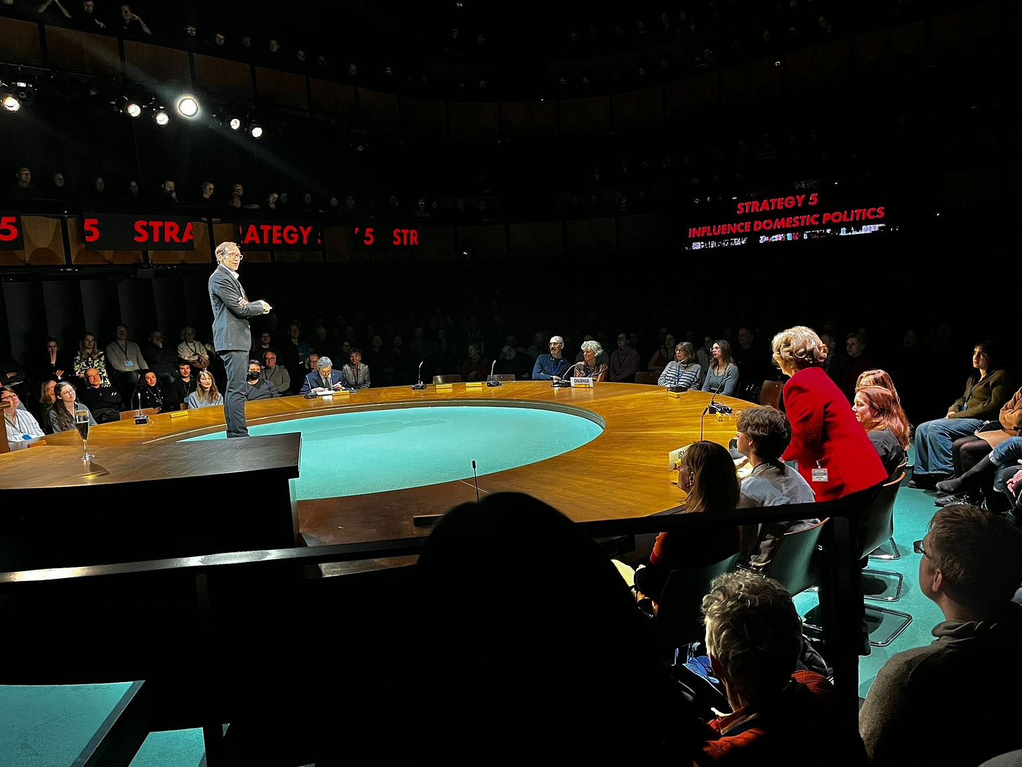 Photo of a man standing on circular stage with people around him