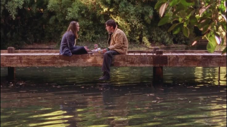 This may contain: two people are sitting on a dock in the water