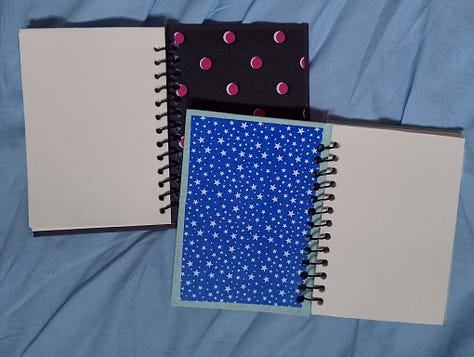 Grade de fotos mostra quatro cadernos, um preto, um azul com carimbos azul escuros em formato de caveira, um rosa com um gato preto pintado e um marrom com carimbos azuis de um peixe com pernas