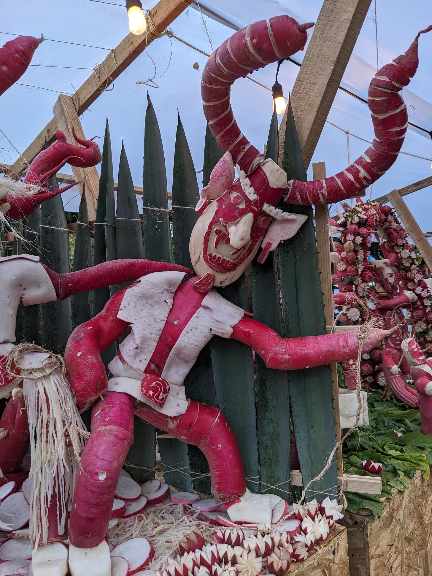 A demon with giant red horns and white jumper is roughly carved out of red and white radishes.