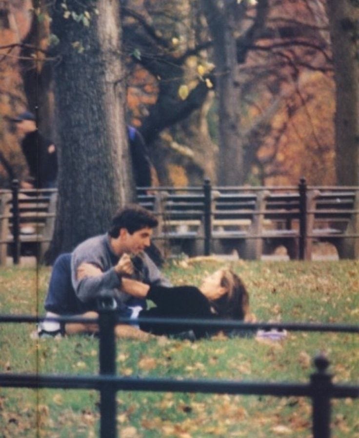 This may contain: two people are sitting on the ground in a park, one is touching the other's chest