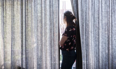Profile of a woman looking out of a window between drawn curtains