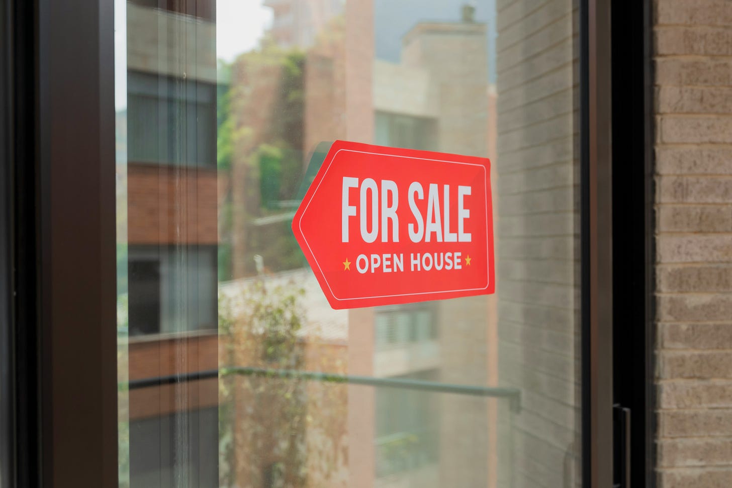 A red sign on a glass door that says FOR SALE OPEN HOUSE