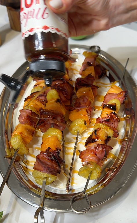 Whipped lime ricotta spread across a silver oval platter, Finished grilled mortadella, cantaloupe, and gnocchi skewers with whipped ricotta and pistachios on a silver platter being topped with hot honey