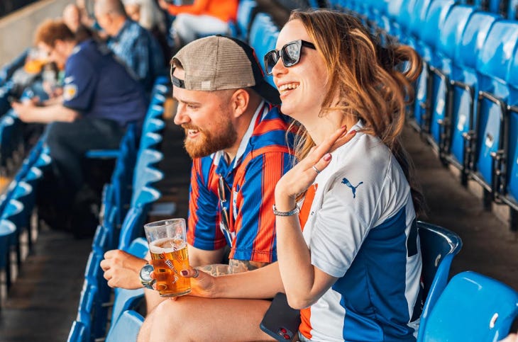 Two people sitting in blue seats in a football stand with glasses of beer in their hands Two people sitting in blue seats in a football stand with glasses of beer in their hands