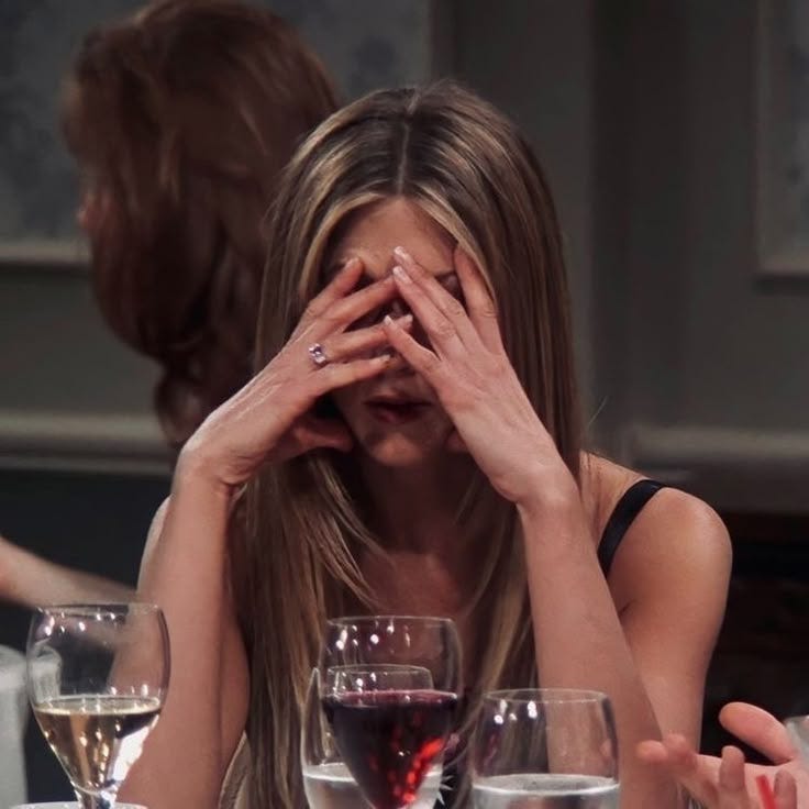 This may contain: a woman covering her eyes while sitting at a table with several wine glasses on it