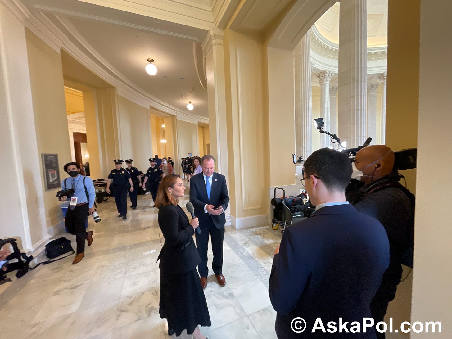 A TV reporter prepares to interview a politician on camera as Police Officers walk past in background Photo: Matt Laslo © AskaPol.com