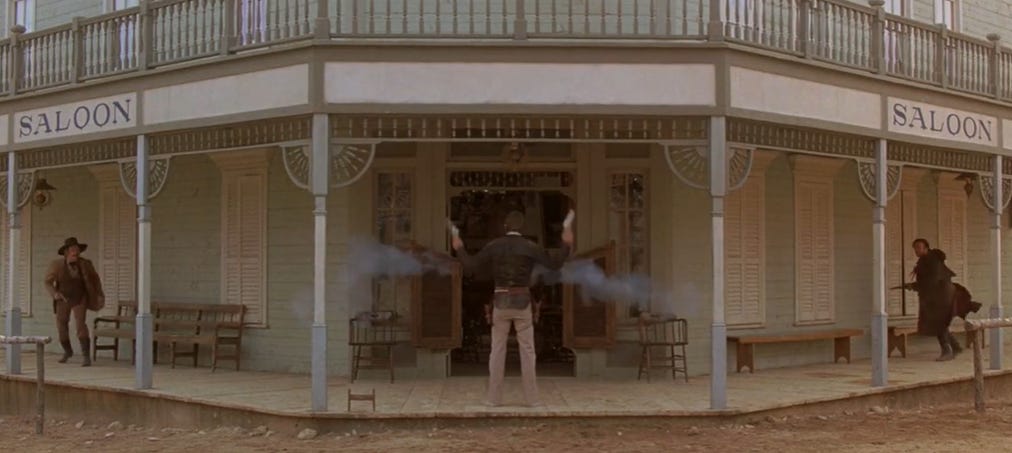 Screen clip from Silverado of Kevin Costner shooting two men on the sidewalk, one to his left, one to his right.