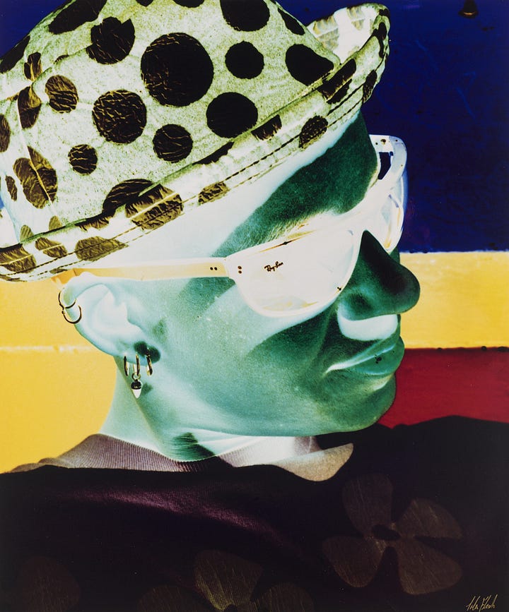 1) Inverted color portrait of Lola with curly hair, head tilted, in a white top against a dark background, creating an abstract, serene atmosphere. They are holding something in their lap that resembles a penis. 2) A negative-style image of Lola in a polka-dot hat and sunglasses. Lola has multiple earrings and a calm expression, with a colorful abstract background.