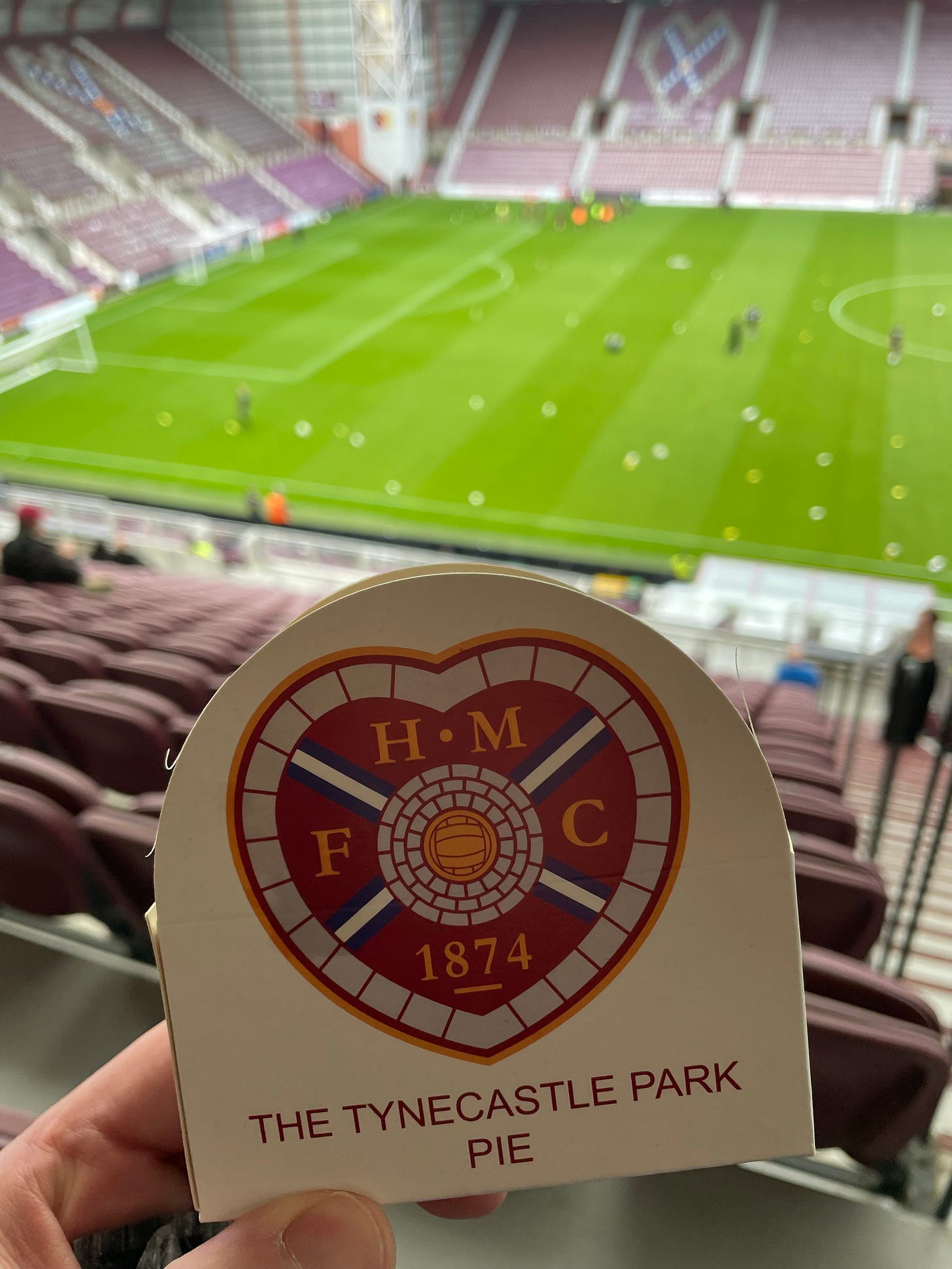 Ben's pie in a cardboard pie-case, with the green pitch in the background