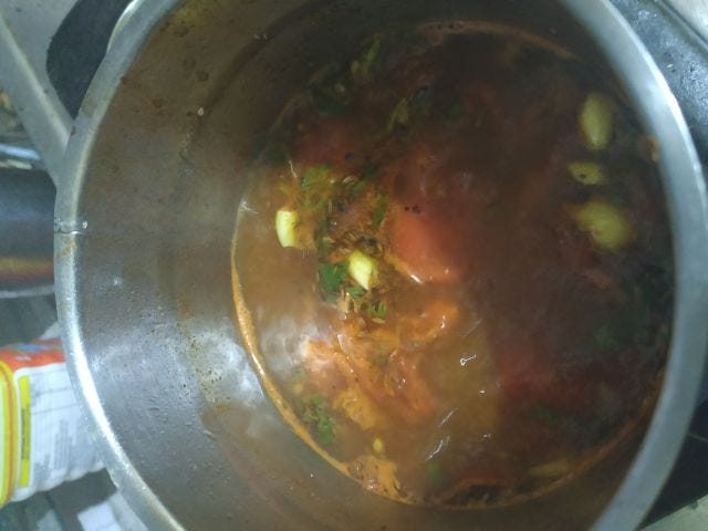 A metal bowl filled with brown juice with floating tomatoes and garlic.