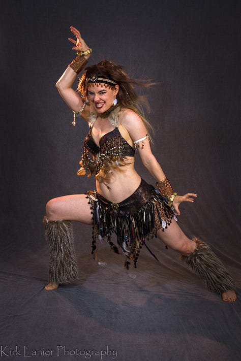 Two mirror-selfies on the green screen floor: a drab brown and olive ratty hunting outfit and a pretty-in-pink-and-sand pants and tunic outfit. And a pro shot of my She-Wolf fur and feathers wild-woman outfit in a dynamic, claw-handed pose with leg poised to kick and gaze aimed and fixed.