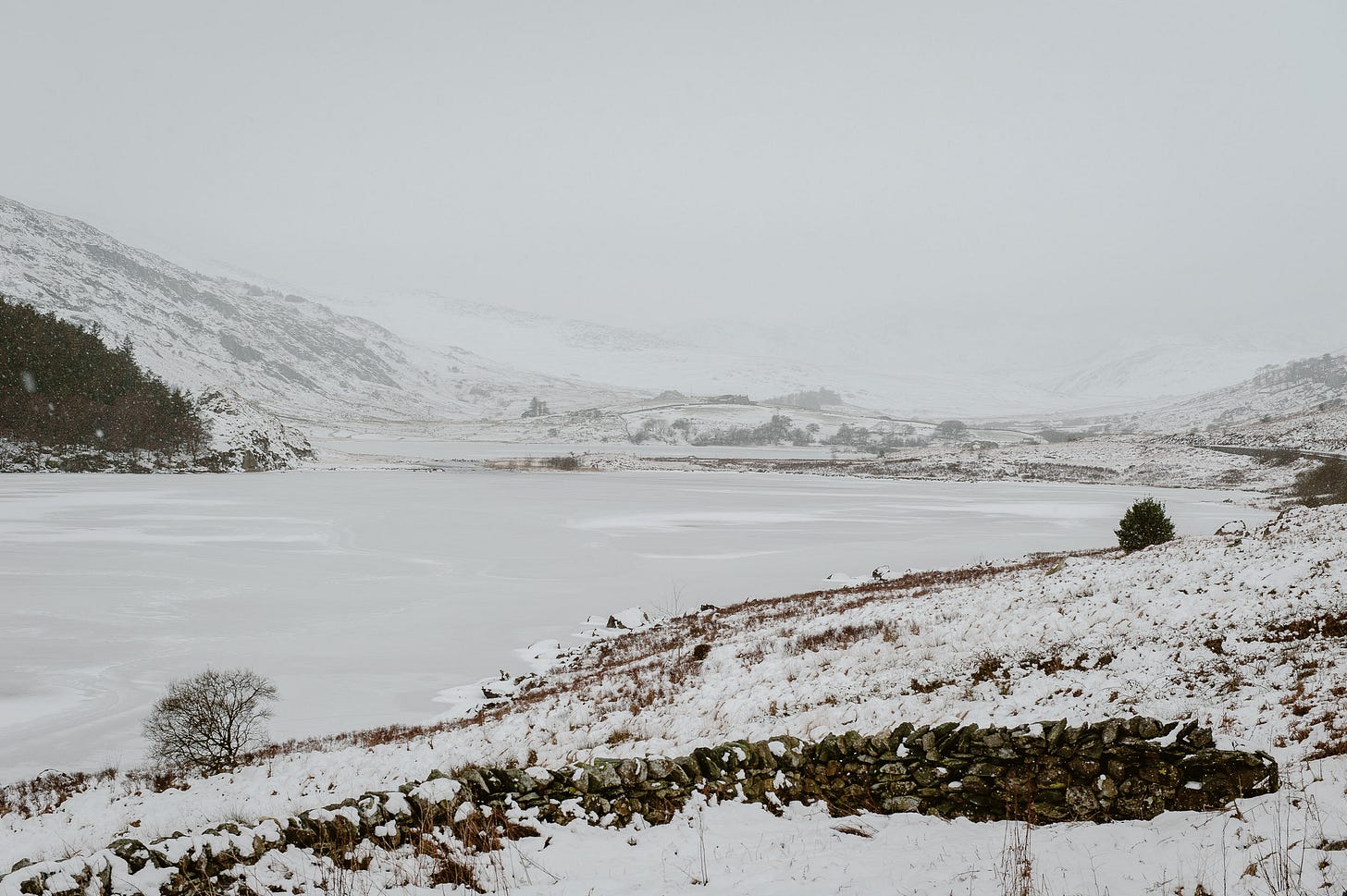 A frozen snow-covered lake sits amongst snowy hills and mountains.
