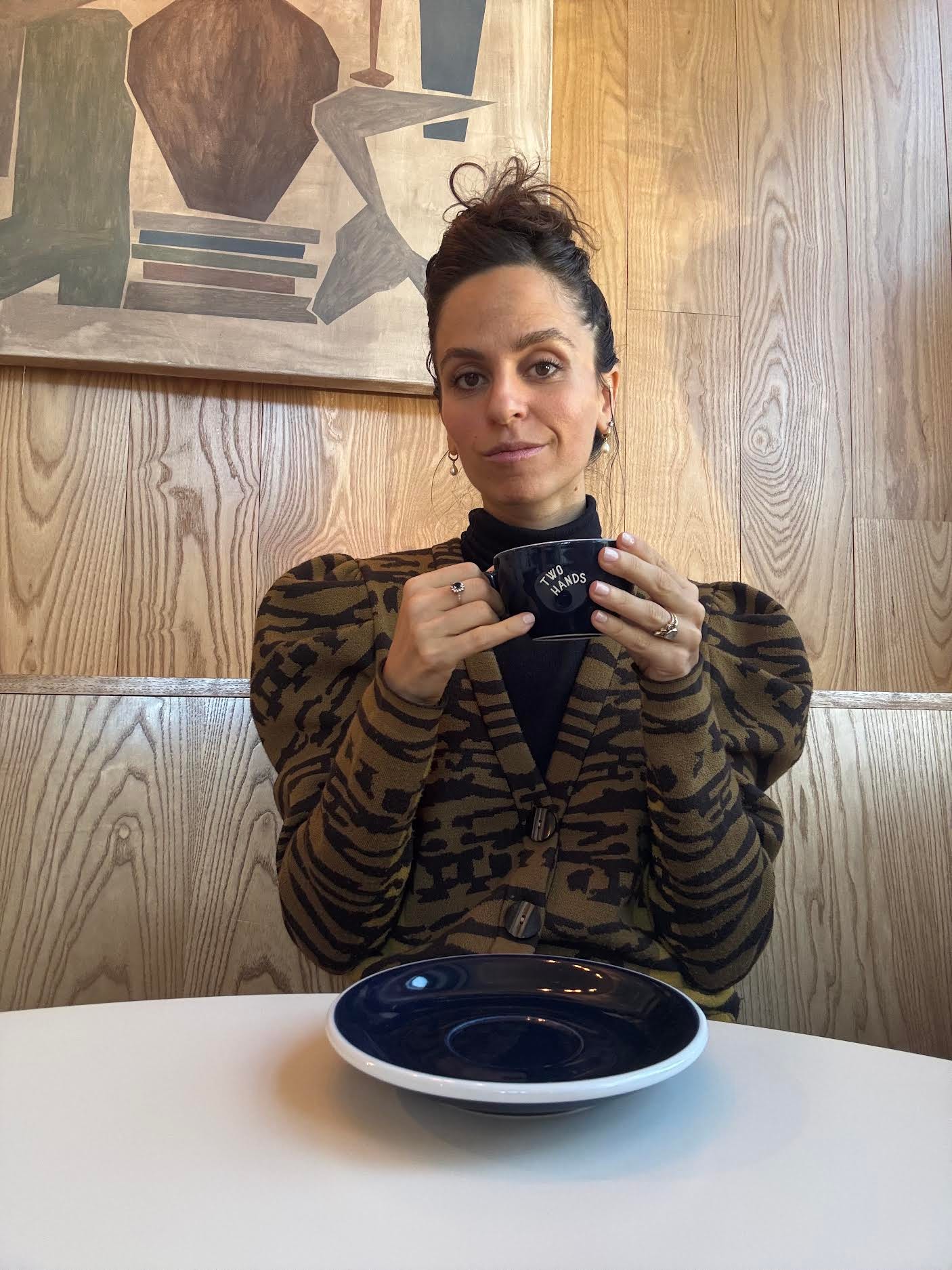 Elian Monjack wearing an animal print jacket holding a coffee cup that says 'two hands'