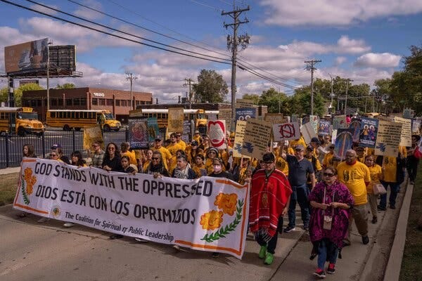 A crowd of people, many wearing yellow T-shirts, marching down a road holding a white banner. A crowd of people, many wearing yellow T-shirts, marching down a road holding a white banner.