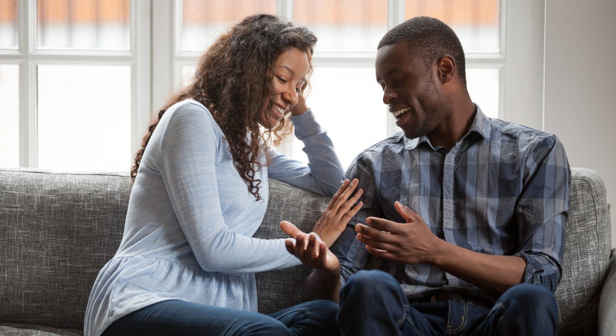black husband and wife sitting on a grey sofa engaged in conversation