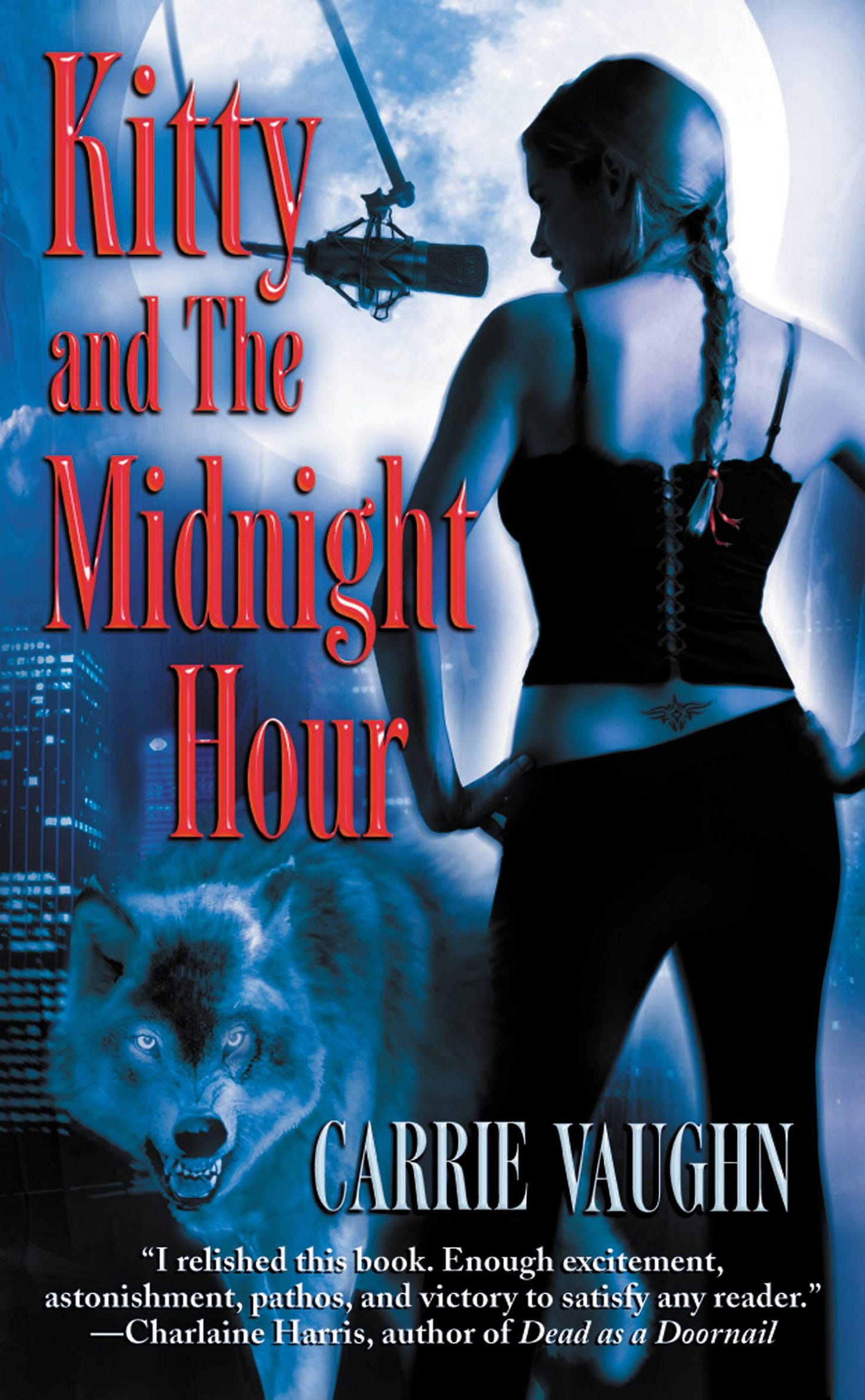 Book cover for Kitty and The Midnight Hour by Carrie Vaughn. A woman with a long braid stands in profile beneath a large full moon, facing a suspended studio microphone. She wears a black corset-style top and dark pants, with a small tattoo visible at her lower back. A wolf with glowing eyes appears in the foreground against a nighttime city skyline. The title appears in large red serif letters, and the author’s name is displayed at the bottom.