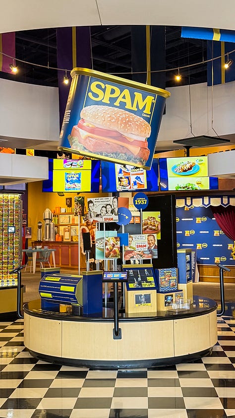 SPAM displays, a wall of colorful SPAM cans, and one person measuring their height against a SPAM can wall