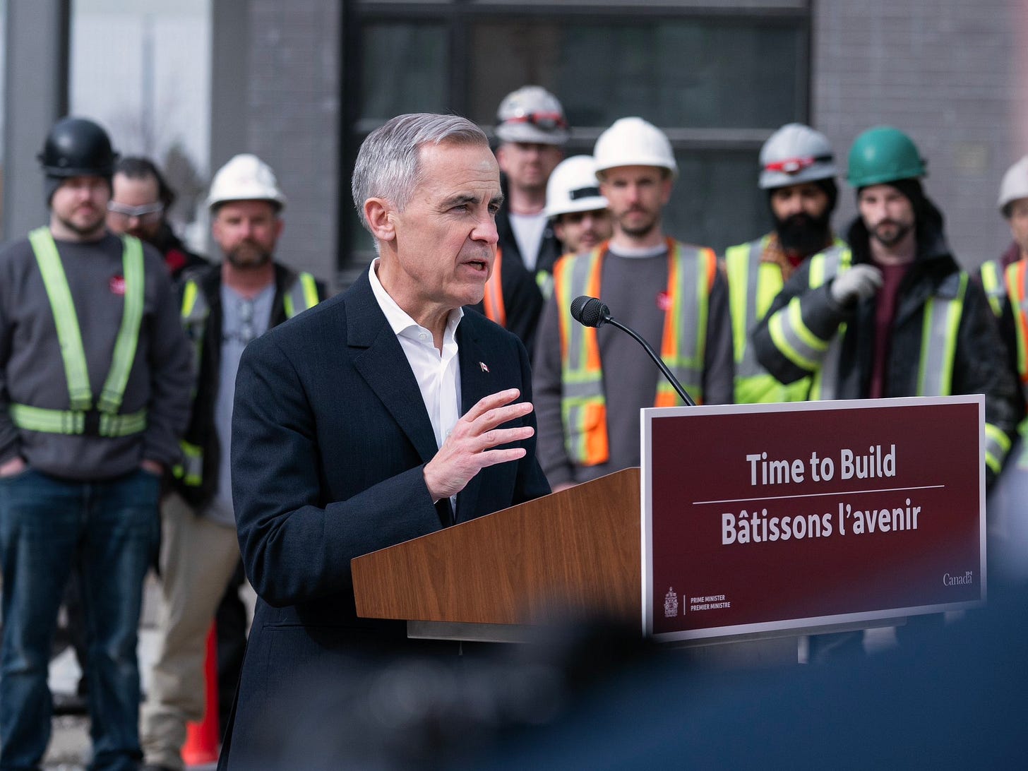 Prime Minister Carney stands at a podium in front of Canadian construction workers.