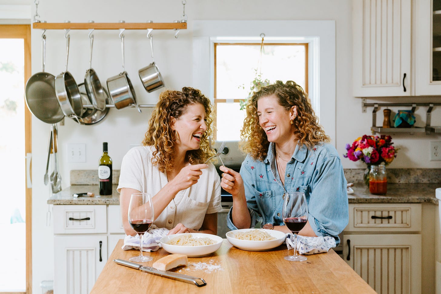 two white women sitting in a kitchen smiling and cheering with forks