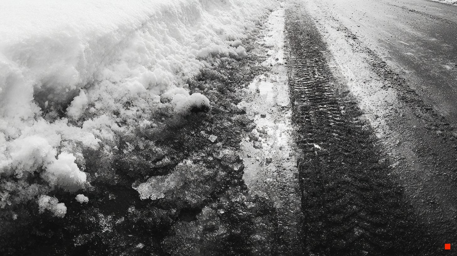 Black-and-white photograph of tire tracks pressed into slushy winter snow along a residential street, with ice, grit, and compressed snow marking the aftermath of movement.