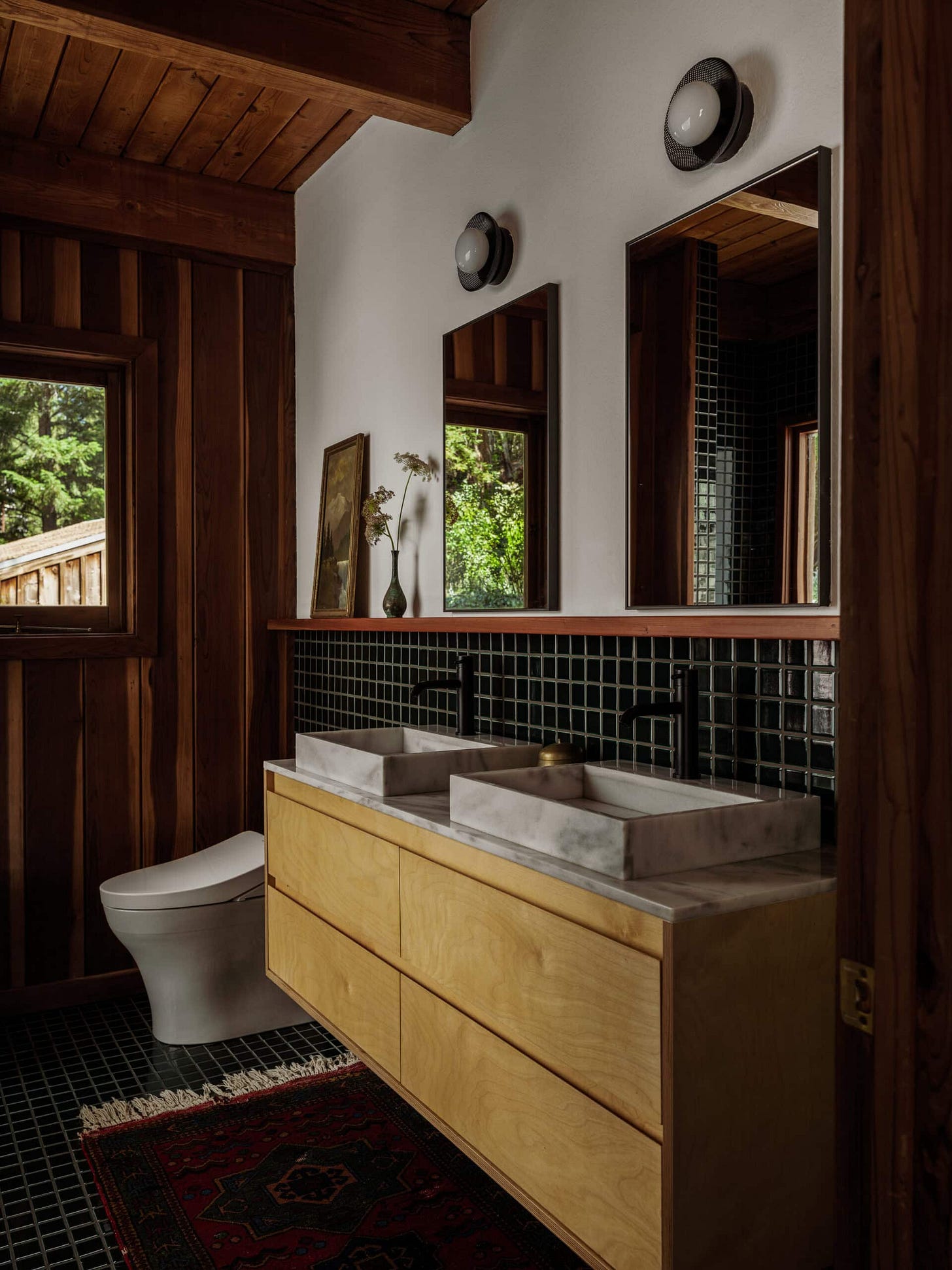 The after of the cabin bathroom features a new birch vanity with a marble top, mesh-wired black sconces, and a floating shelf.  