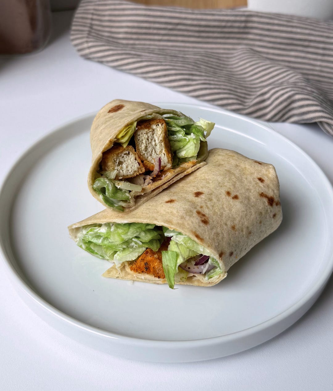 Close-up of a crispy tofu Caesar salad wrap cut in half, showing golden tofu cubes, fresh romaine lettuce, and creamy dressing inside a whole wheat wrap.