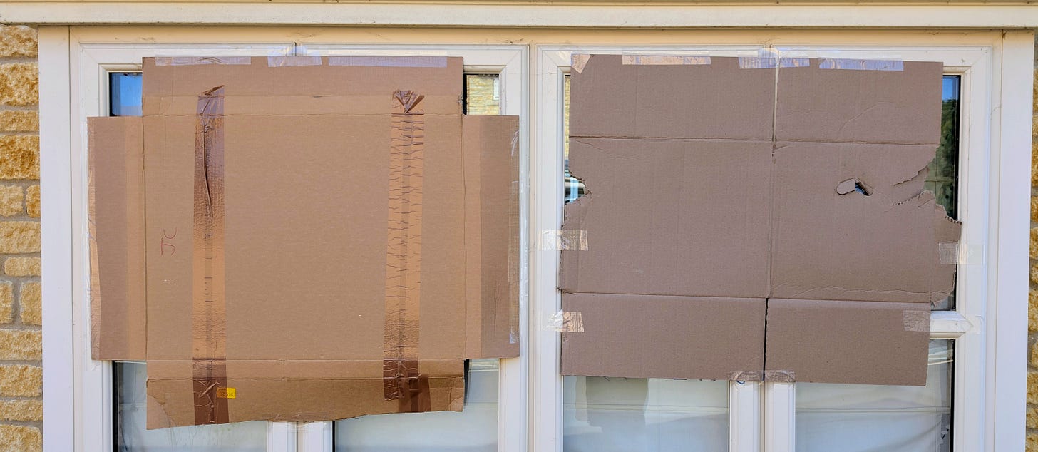 Two windows partly covered by cardboard, inexpertly applied. 