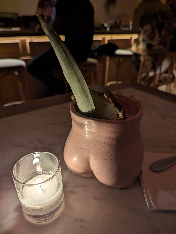 Left to right: An aloe leaf pops out of a glass in the shape of a woman's behind; A small orange peel suspended by a toothpick over a bowl