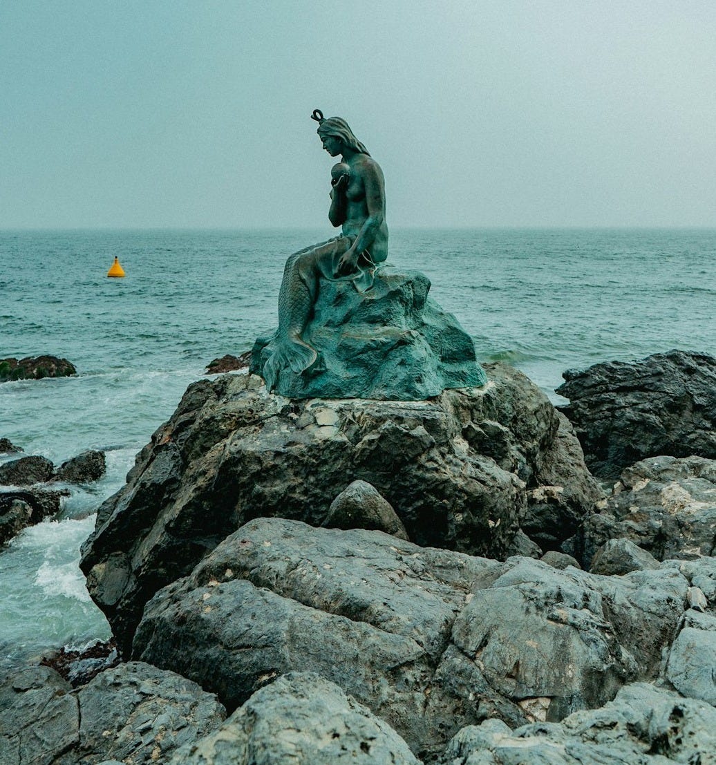 statue of a woman on a rock near the ocean