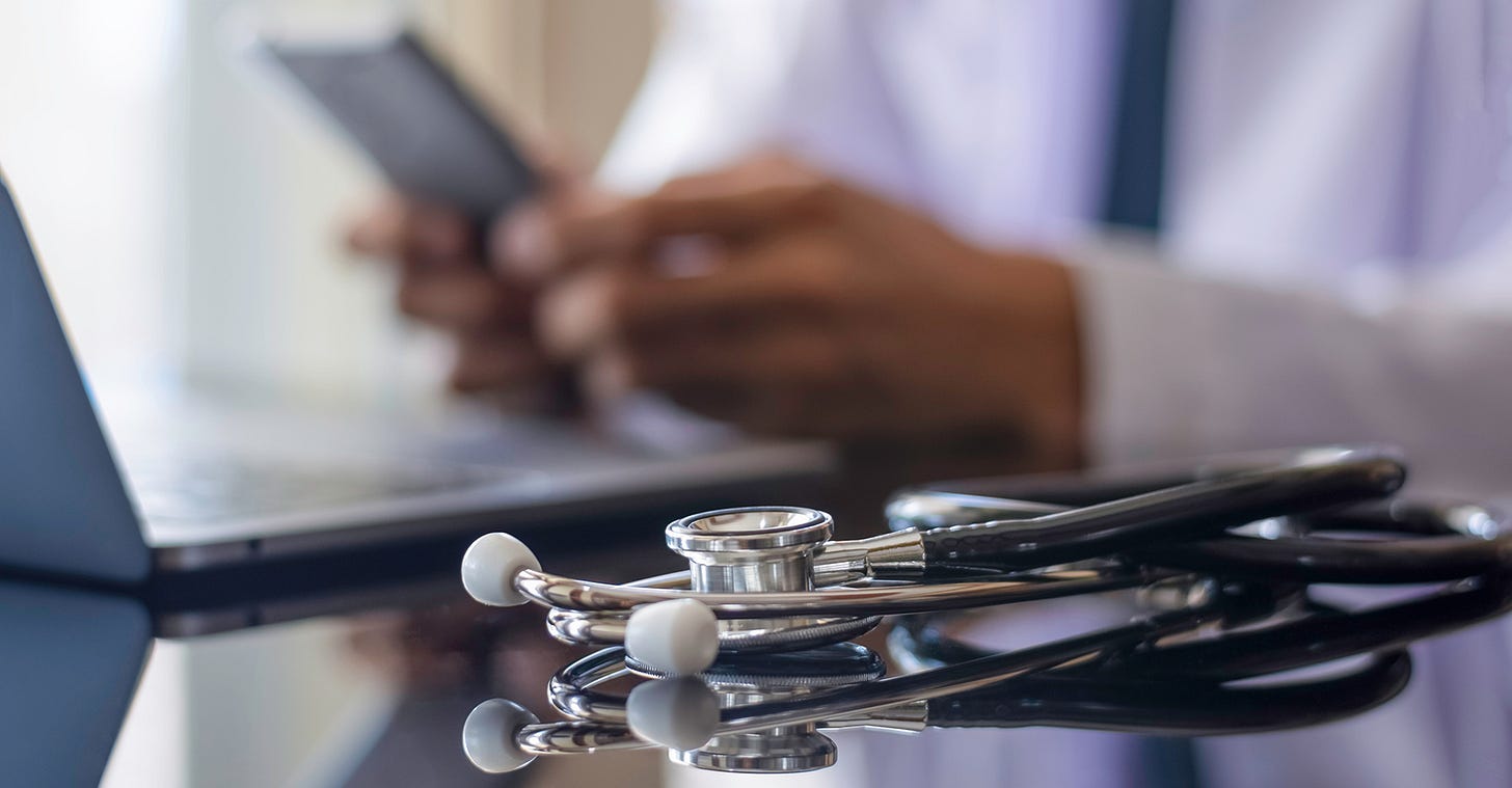 Physician at a computer and phone in the background behind a stethoscope