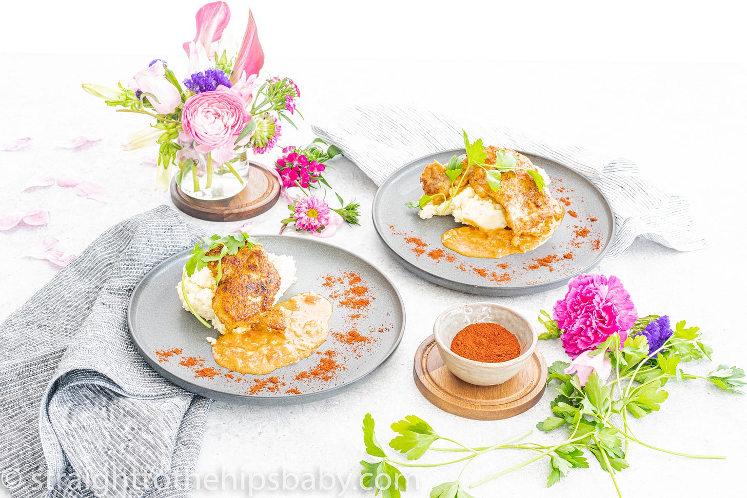 Food on light grey plates with flowers displayed in a glass on the side of the table. 