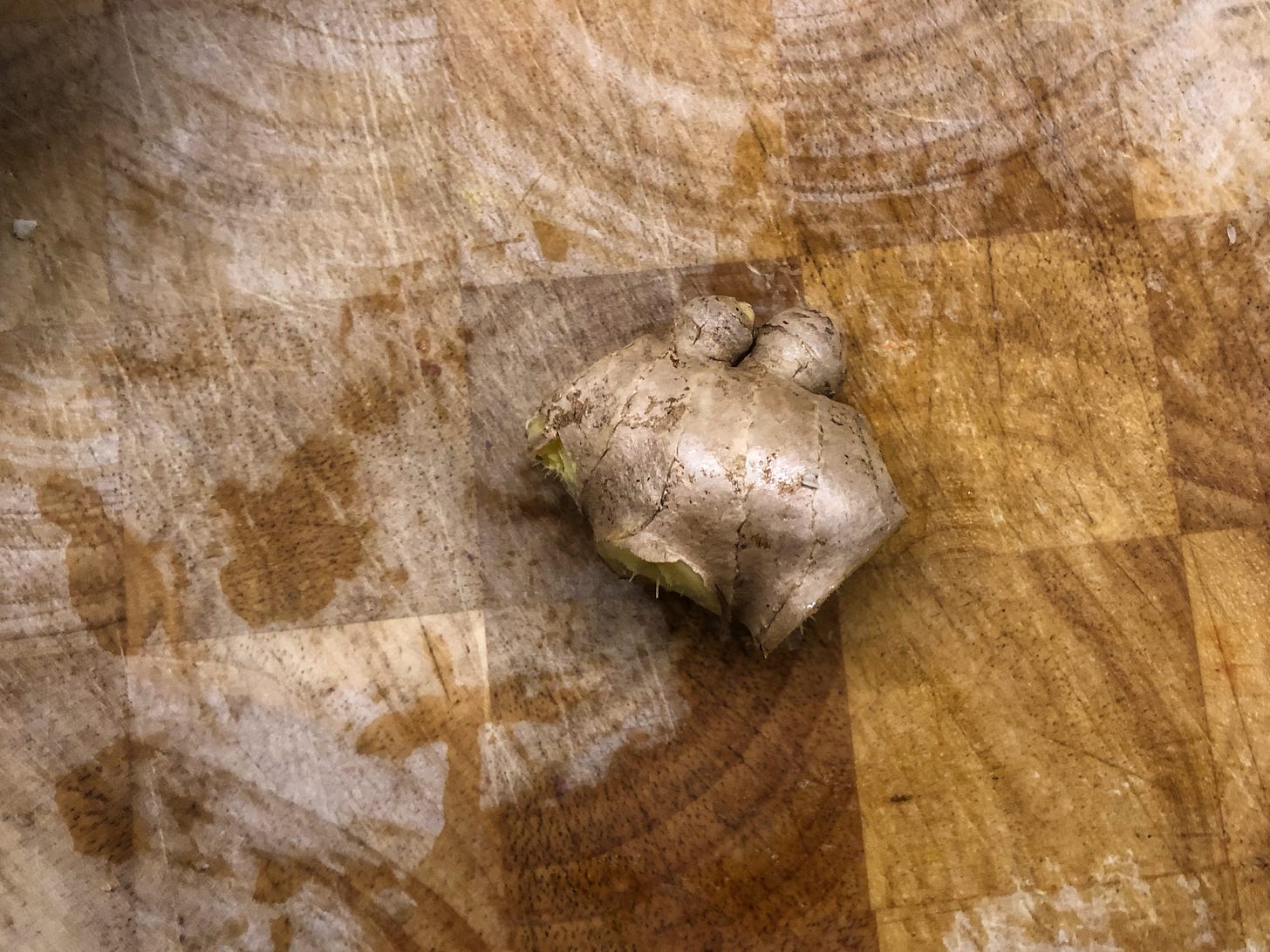 An unpeeled piece of ginger with some knobby protrusions on a cutting board