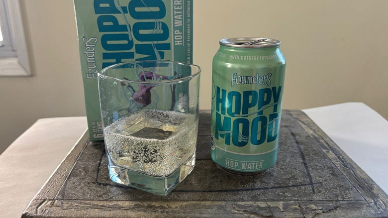 Can and glass of Founders Hoppy Mood hop water on a table with the box behind them Can and glass of Founders Hoppy Mood hop water on a table with the box behind them