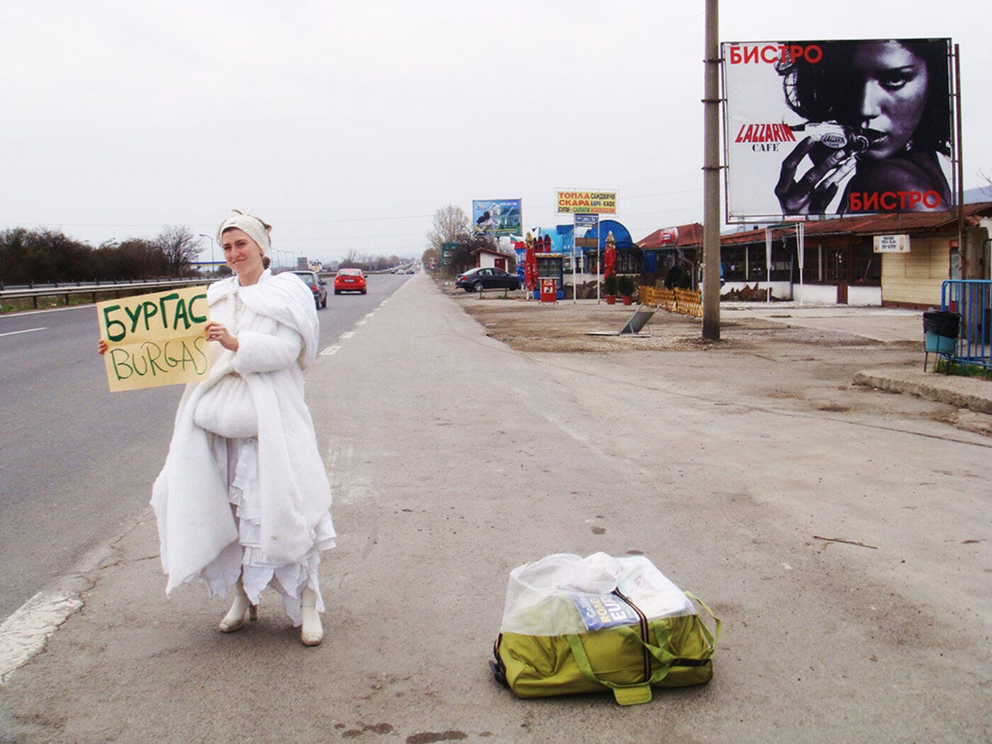 Artist Pippa Bacca standing on the side of a highway wearing a white wedding dress and holding up a paper sign. Artist Pippa Bacca standing on the side of a highway wearing a white wedding dress and holding up a paper sign.