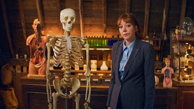 Philomena Cunk (Diane Morgan) standing beside a skeleton in an old fashioned laboratory 
