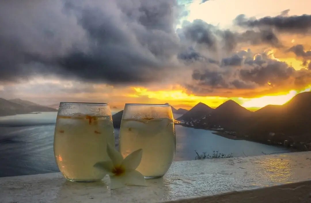 2 cocktails resting on a wall with a sunset in the background